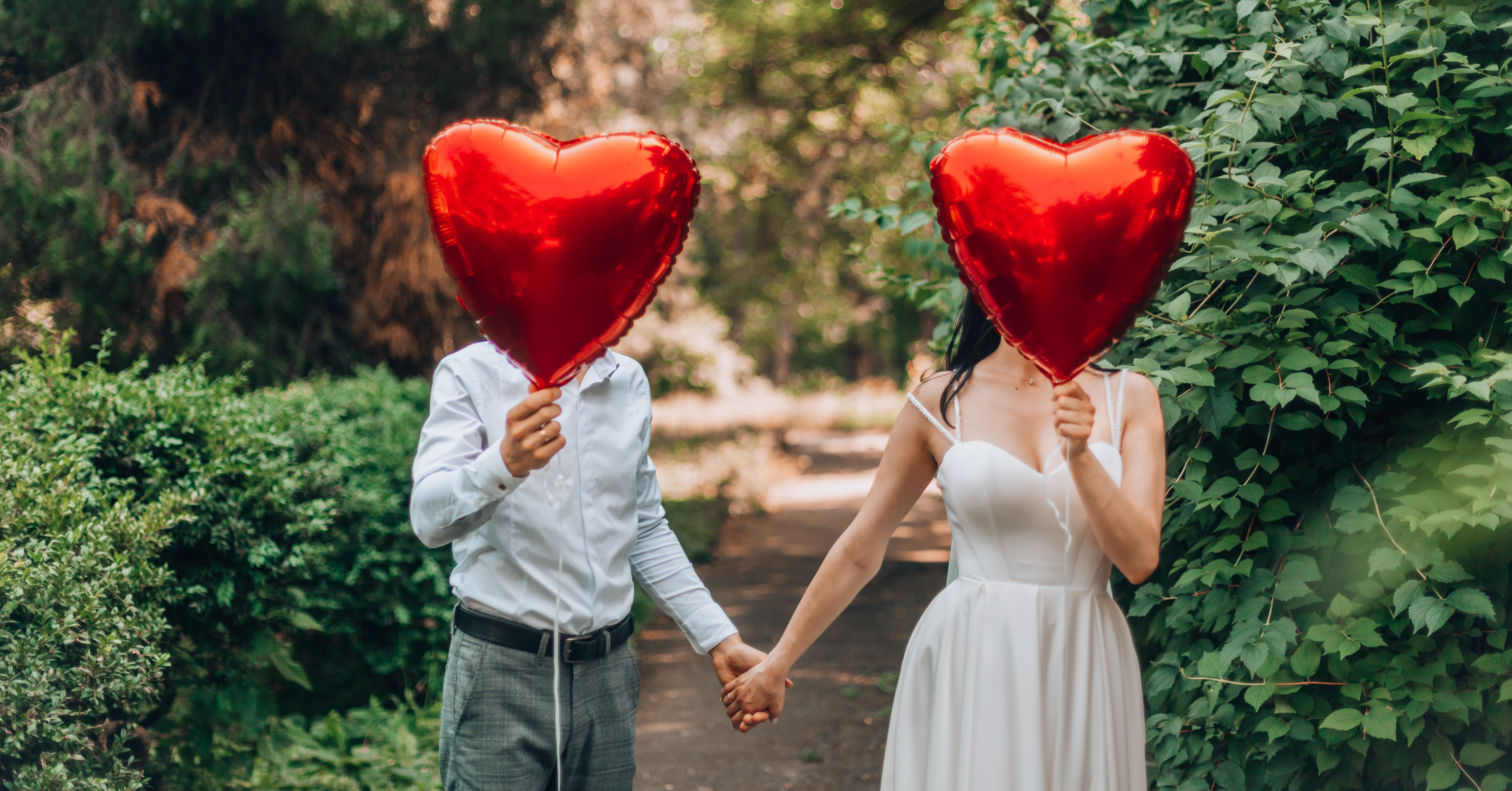 Romantic couple with anxious attachment covering their faces with heart shaped balloons. 
