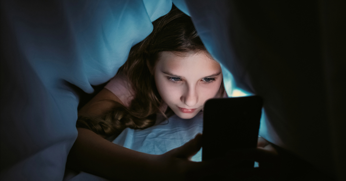 young girl under covers facing tablet blue screen