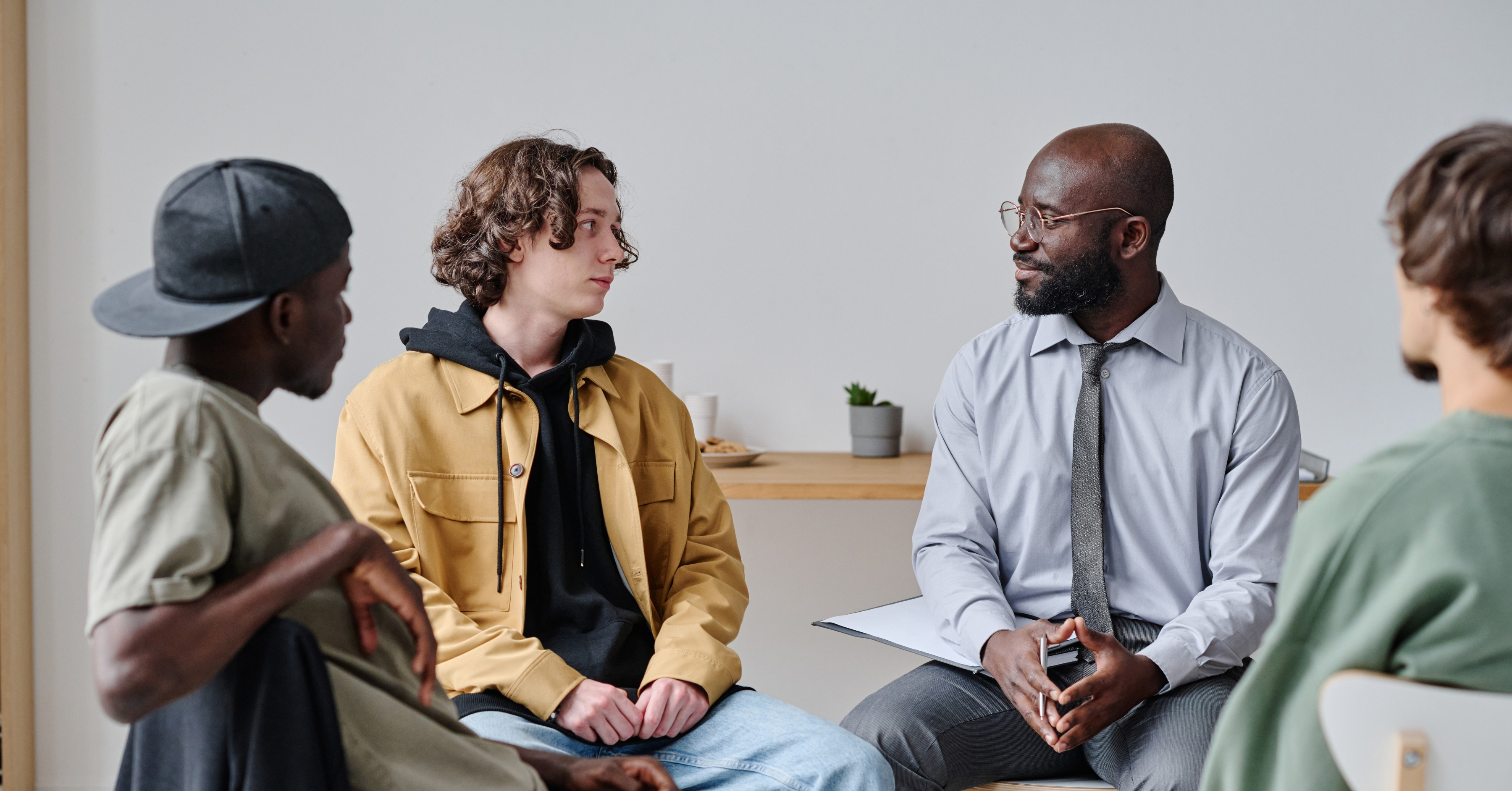 Men's therapy group with young adult male chatting with older man in tie