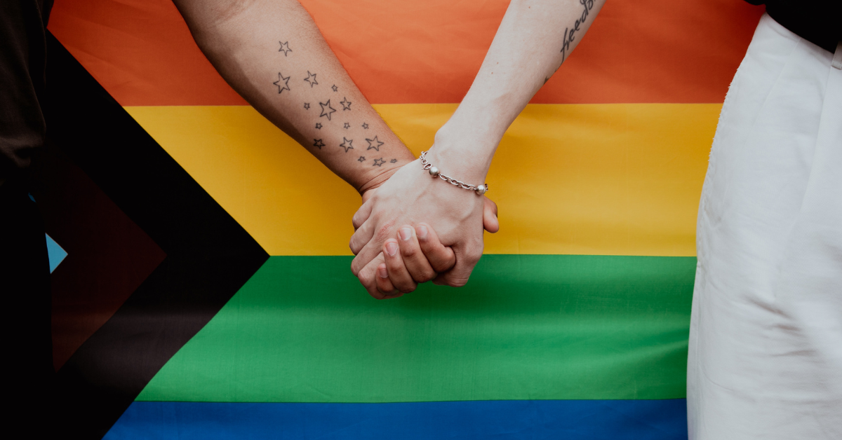 LGBTQ+ strong hands clasping in front of rainbow flag