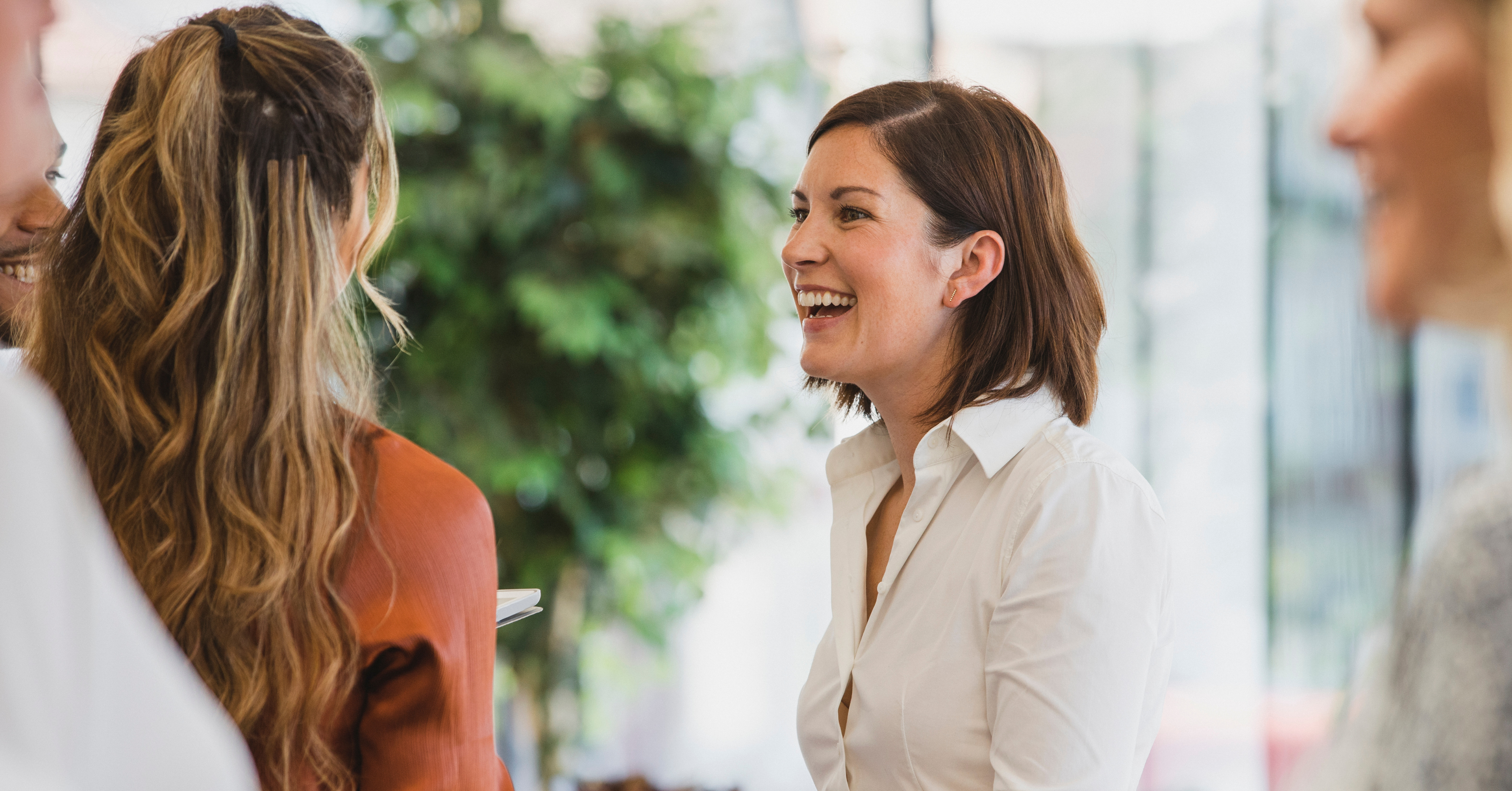 Cheerful women community partners gather at an open house with bright light and green trees