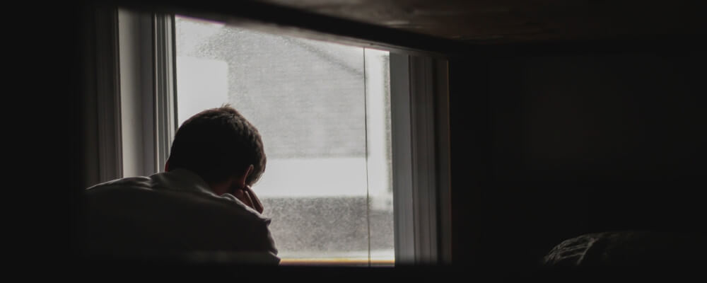 Man looking out window, gloomy. Photo by <a href=