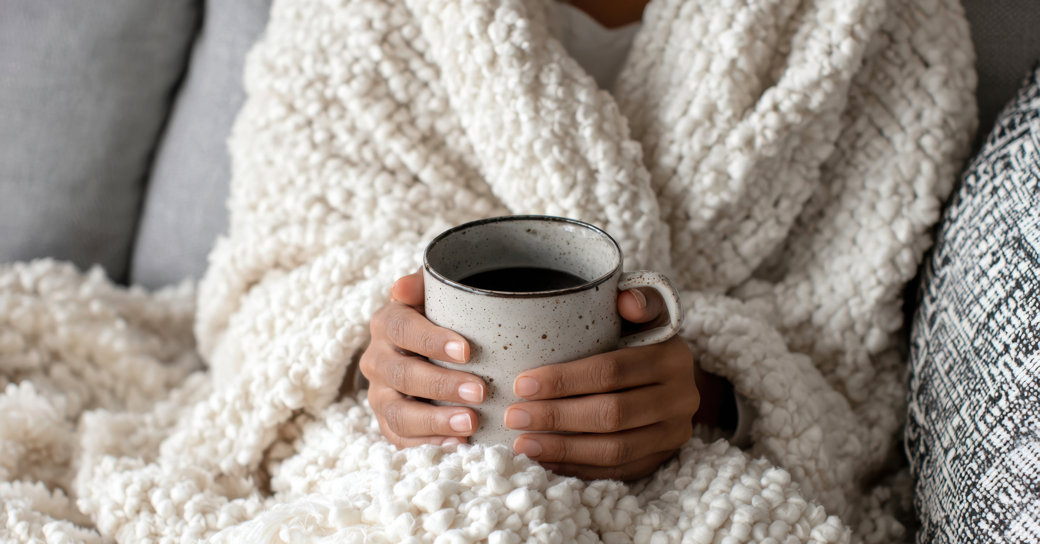 close up hands holding coffee wrapped in layers of blankets