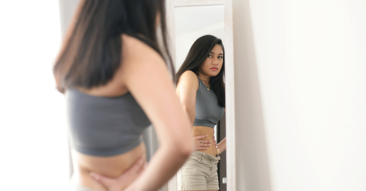 hunched teen girl scowling and facing mirror